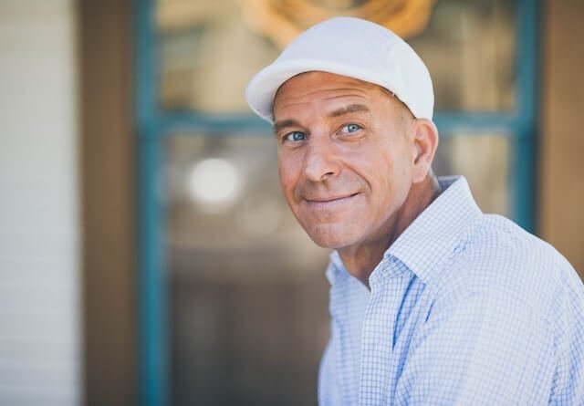 Side profile photo of a man with light blue eyes and wearing a white cap.